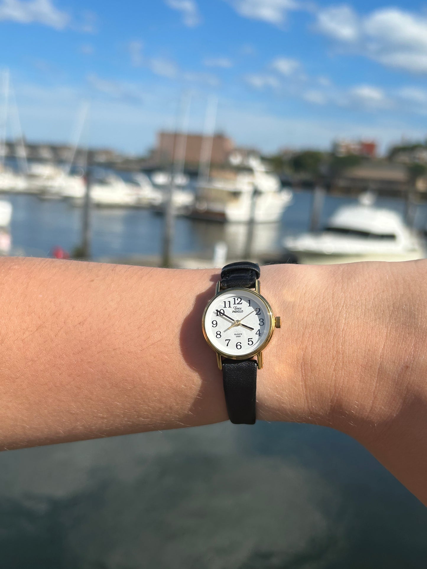 A wrist adorned with the 1999 Timex Gold Case Indiglo Quartz Watch, featuring a white dial and black leather strap.